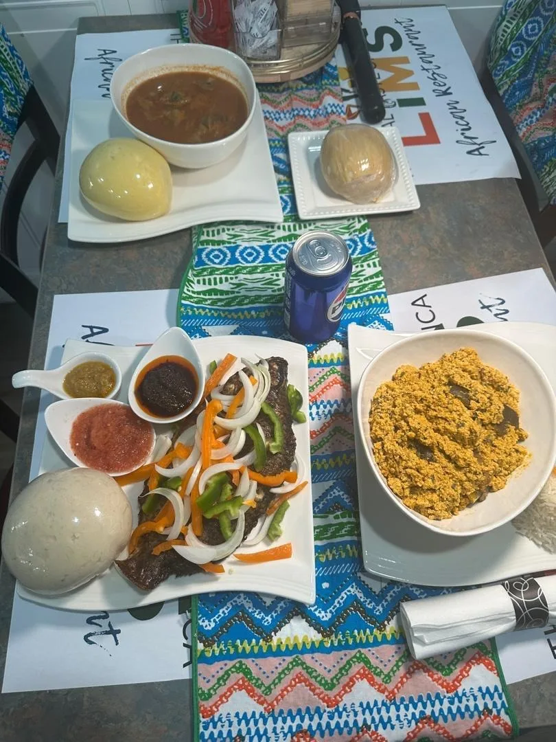 A LIMS table set with fufu and light soup, kenkey, grilled tilapia with peppers and a bowl of egusi